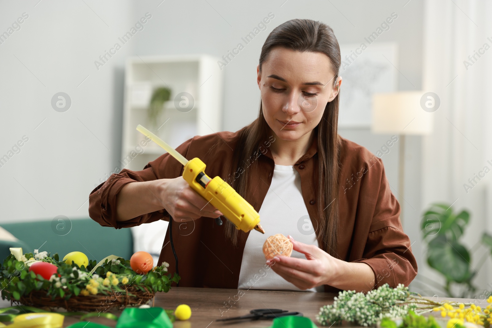 Photo of Woman with hot glue gun making craft at table indoors