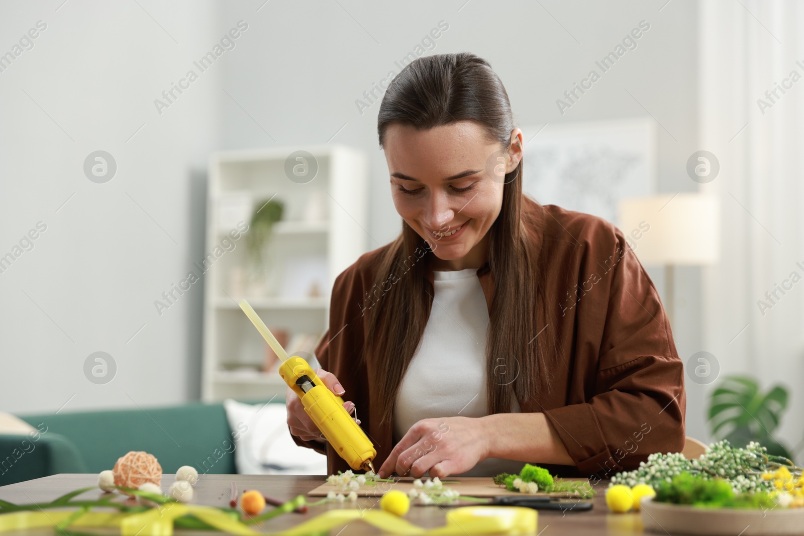 Photo of Woman with hot glue gun making craft at table indoors