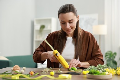 Photo of Woman with hot glue gun making craft at table indoors