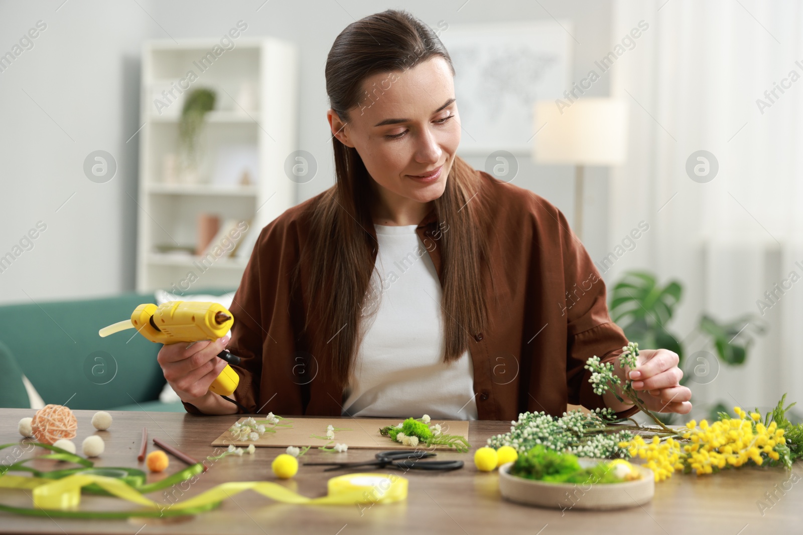 Photo of Woman with hot glue gun making craft at table indoors