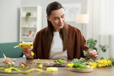 Photo of Woman with hot glue gun making craft at table indoors