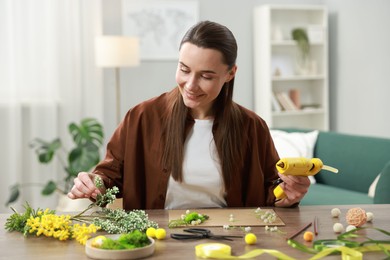 Photo of Woman with hot glue gun making craft at table indoors