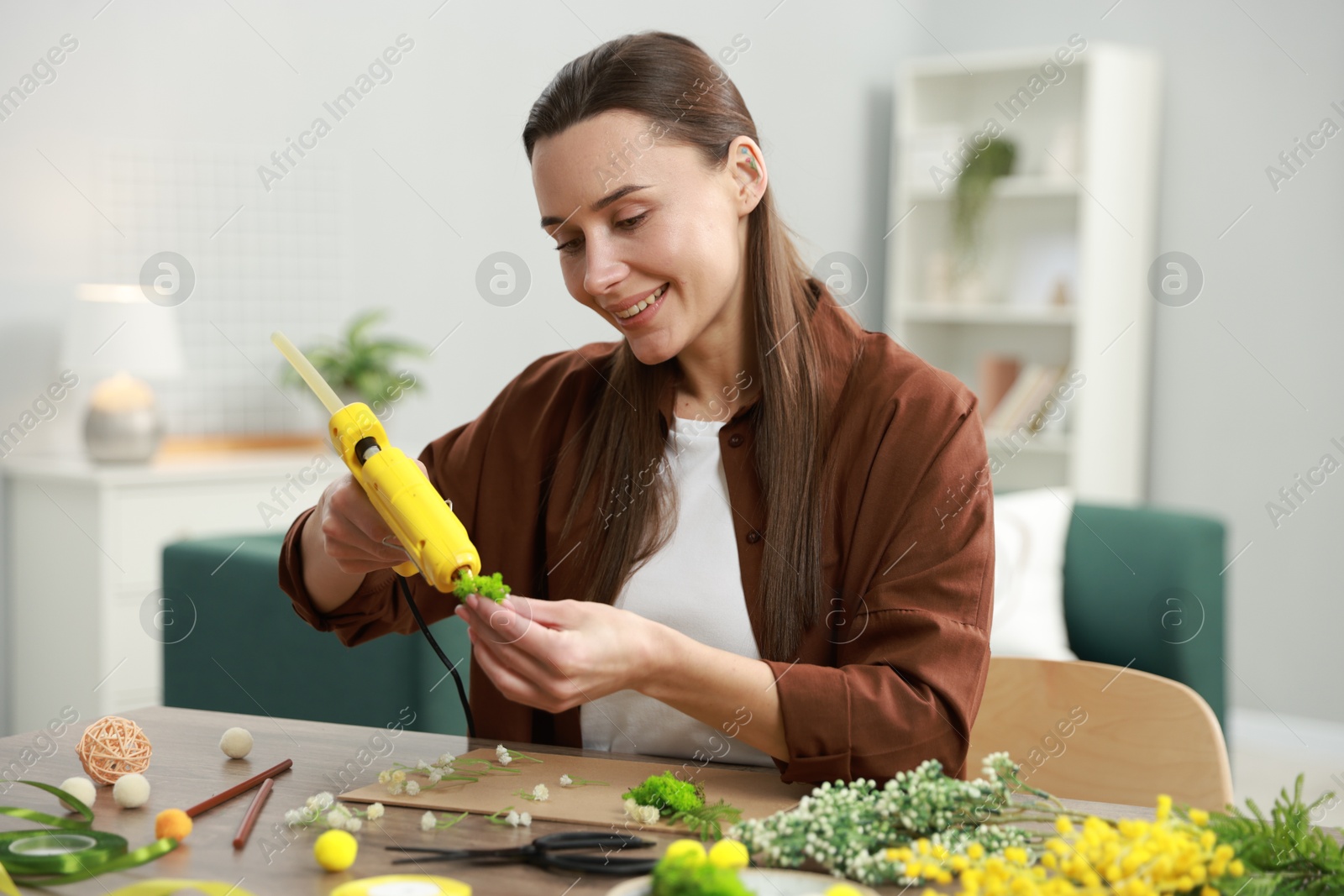 Photo of Woman with hot glue gun making craft at table indoors