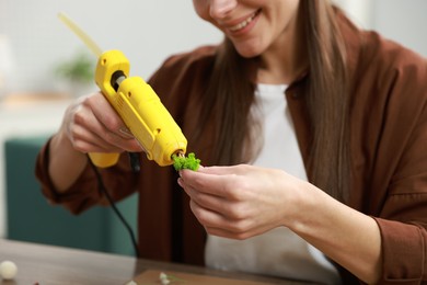 Photo of Woman with hot glue gun making craft at table indoors, closeup