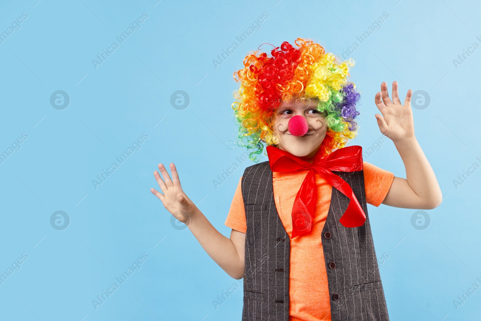 Photo of Happy little boy dressed like clown on light blue background, space for text. Surprise party