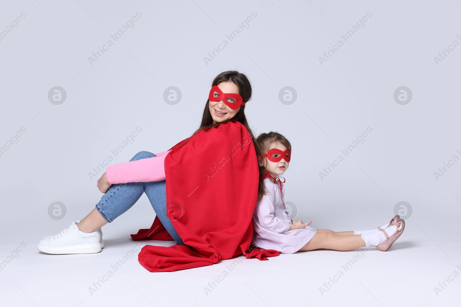 Photo of Mother and her cute little daughter wearing superhero costumes on white background