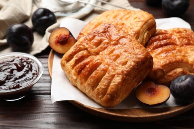 Photo of Delicious puff pastries, jam and plums on wooden table, closeup