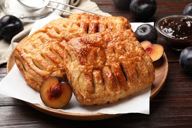 Photo of Delicious puff pastries, jam and plums on wooden table, closeup