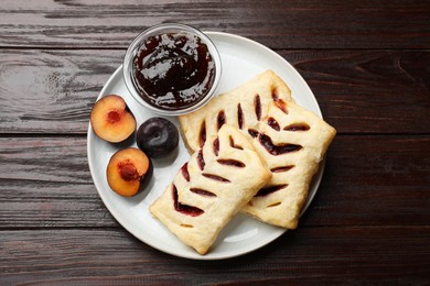 Photo of Delicious puff pastries, jam and plums on wooden table, top view