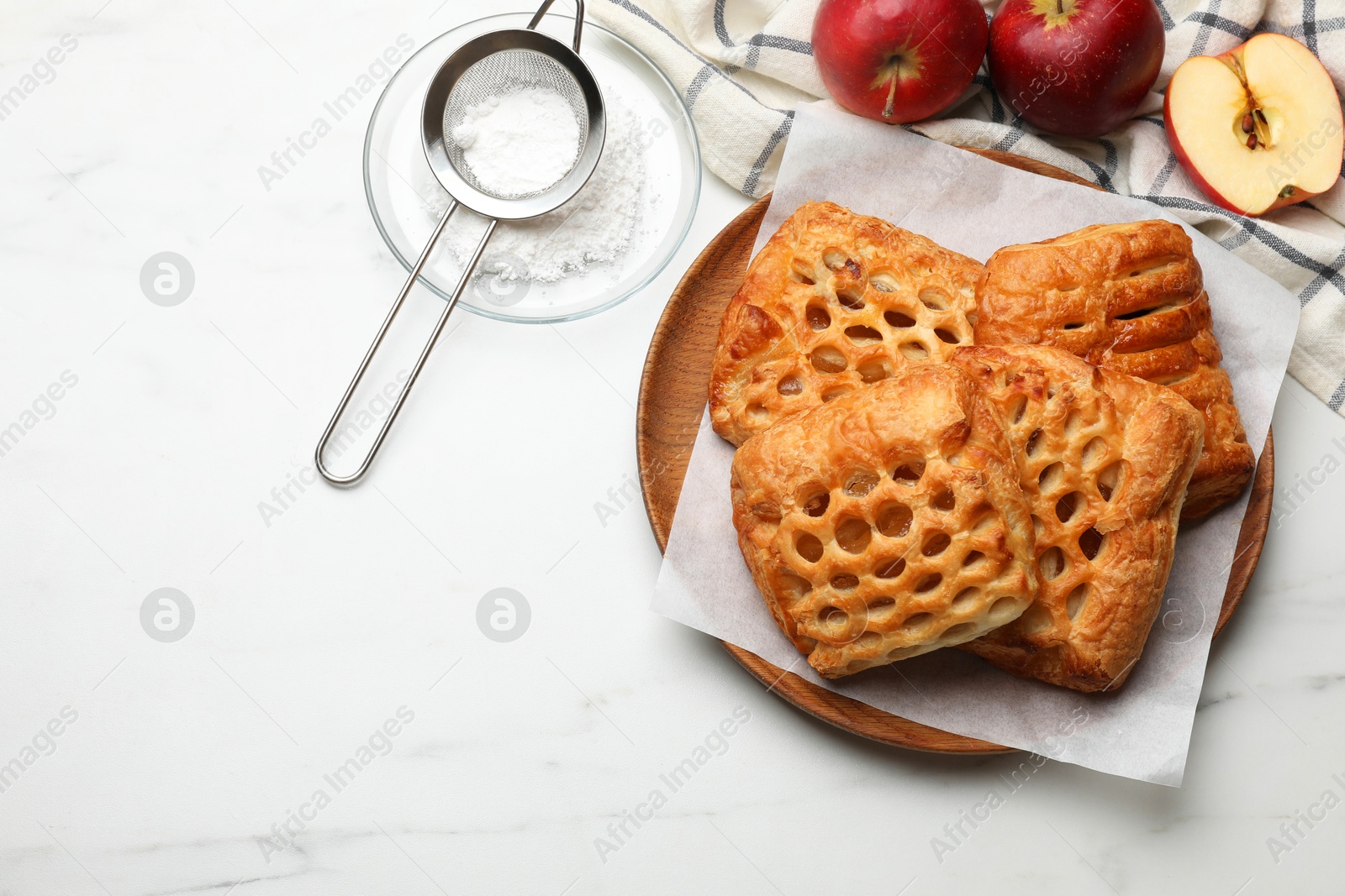 Photo of Delicious puff pastries, apples and powdered sugar on white marble table, top view. Space for text