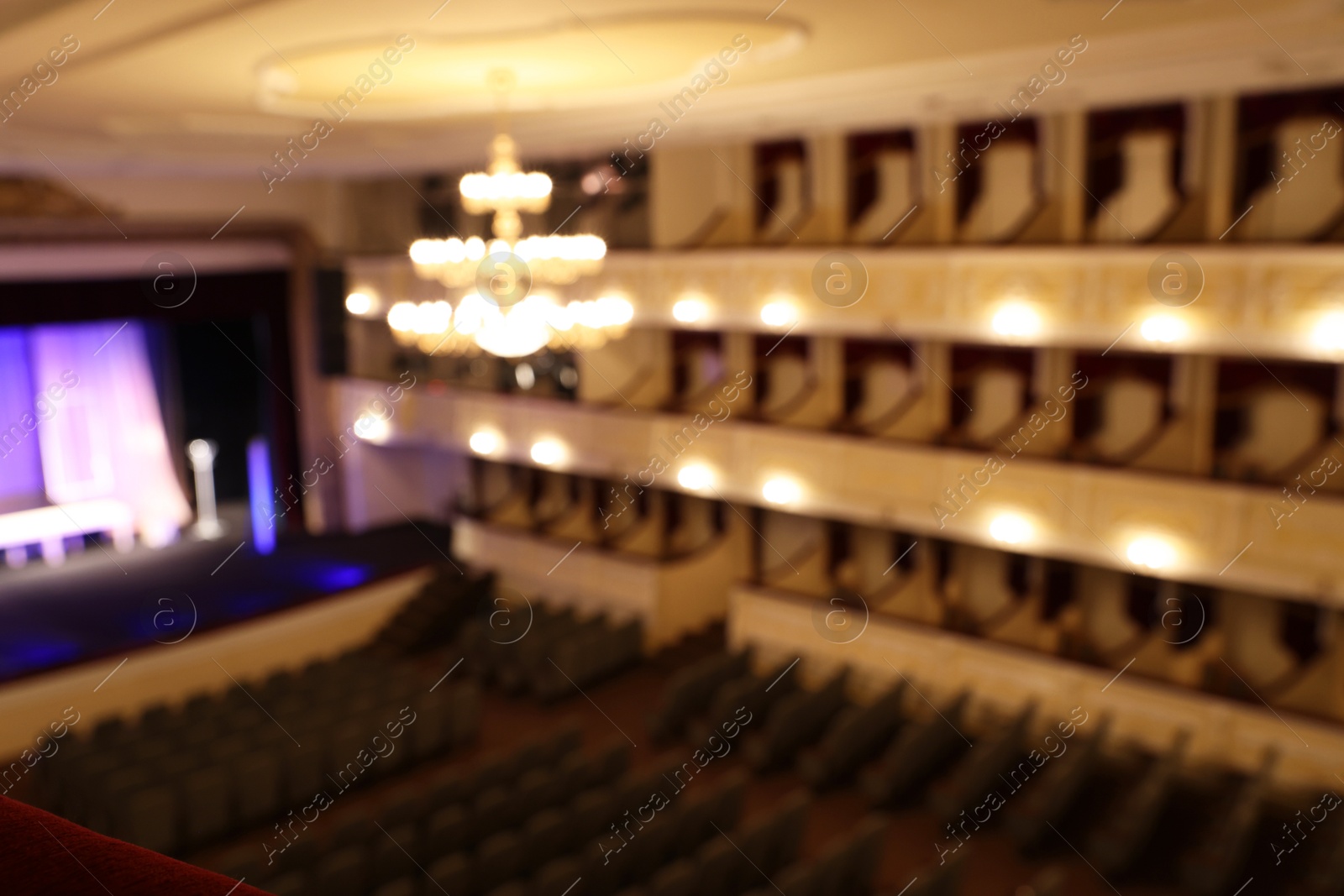 Photo of Blurred view of theatre interior with stage, comfortable seats and beautiful chandelier