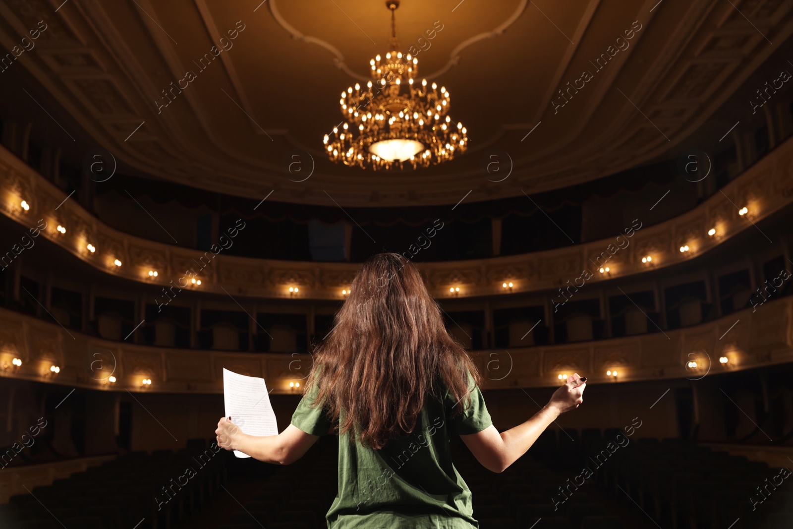 Photo of Professional actress rehearsing on stage in theatre, back view