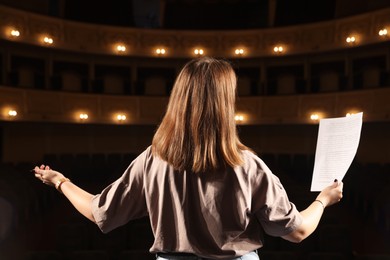 Photo of Professional actress rehearsing on stage in theatre, back view