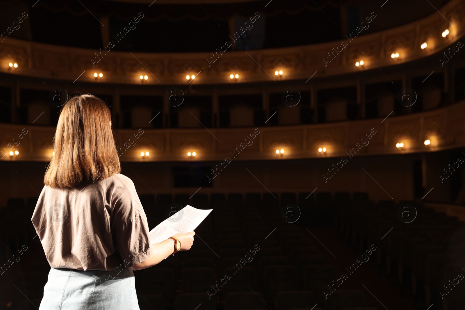 Photo of Professional actress rehearsing on stage in theatre, back view