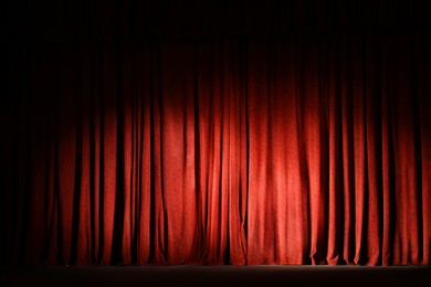 Photo of Elegant closed red curtains illuminated by spotlight in theatre