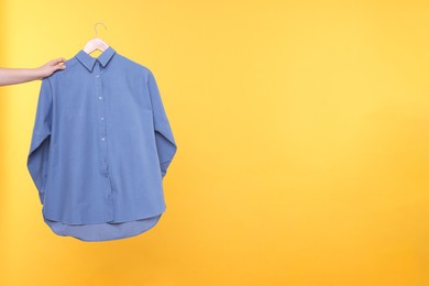 Photo of Woman holding hanger with blue shirt on yellow background, closeup. Space for text