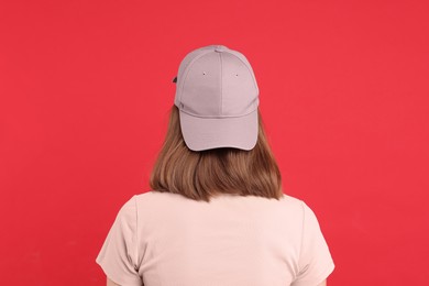 Photo of Woman in stylish baseball cap on red background, back view. Mockup for design