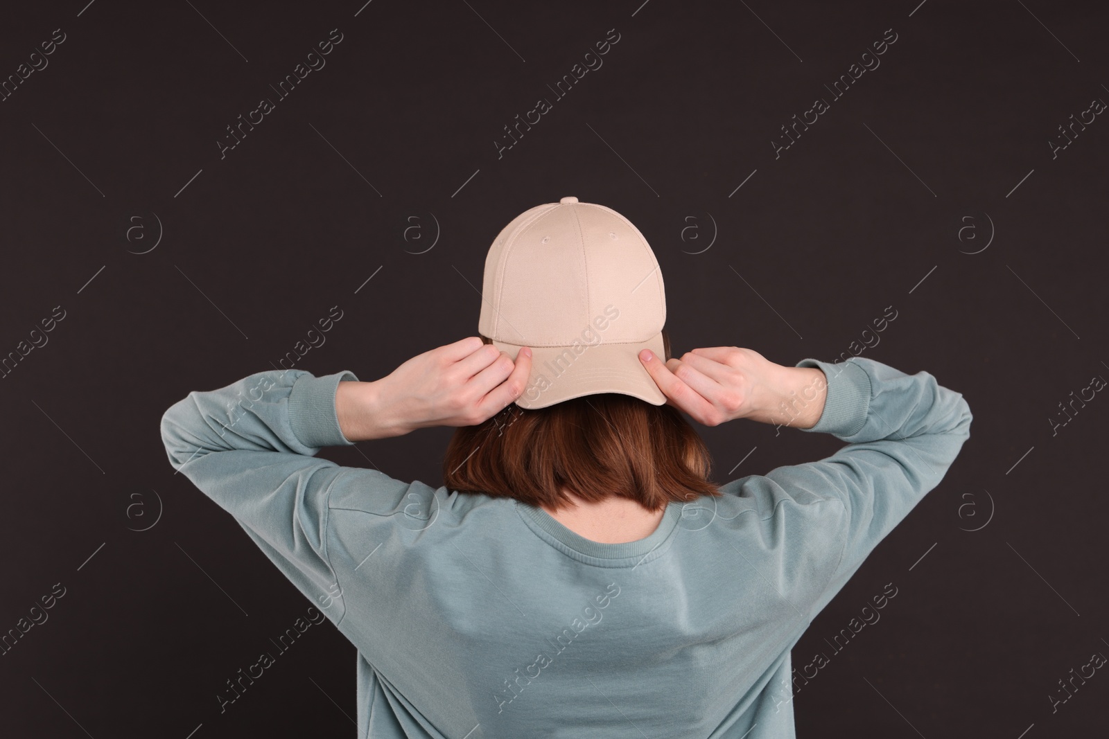 Photo of Woman in stylish baseball cap on black background, back view. Mockup for design