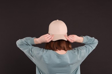 Photo of Woman in stylish baseball cap on black background, back view. Mockup for design