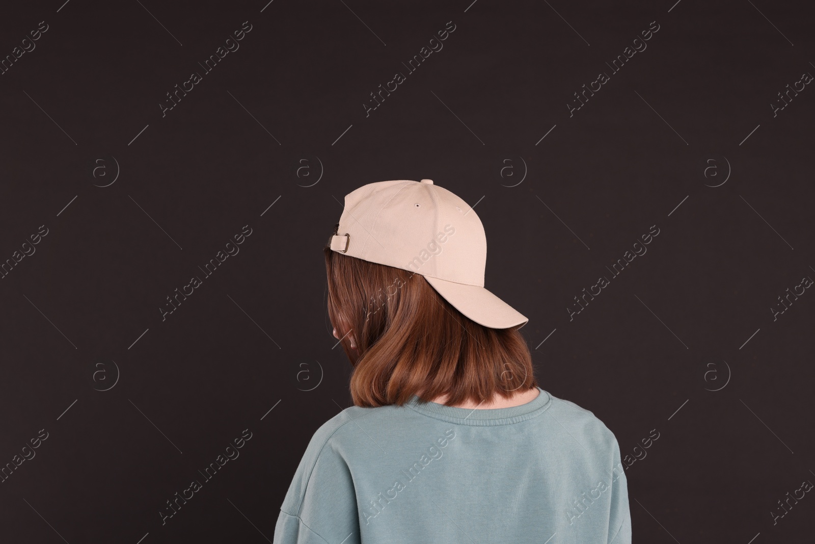 Photo of Woman in stylish baseball cap on black background, back view. Mockup for design