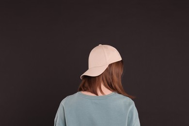 Woman in stylish baseball cap on black background, back view. Mockup for design