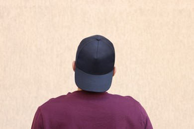 Photo of Man in stylish baseball cap near beige wall, back view. Mockup for design