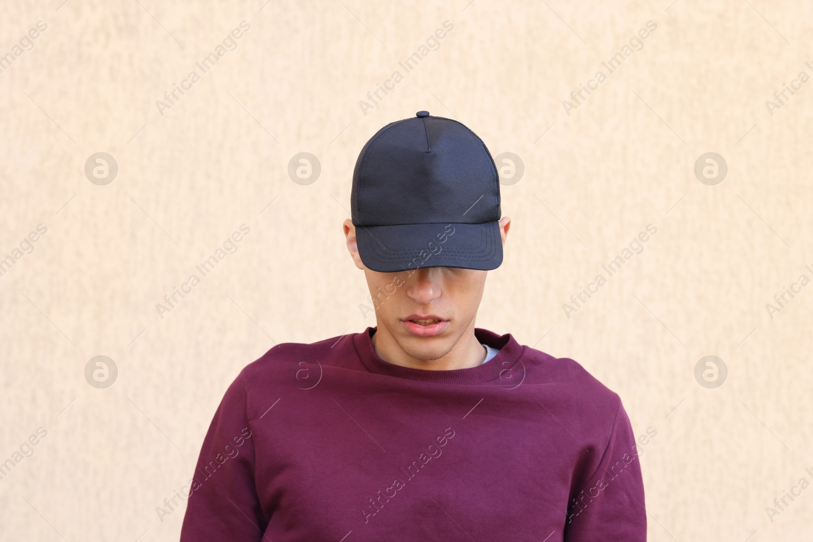 Photo of Man in stylish baseball cap near beige wall. Mockup for design