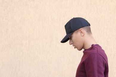 Photo of Man in stylish baseball cap near beige wall. Mockup for design