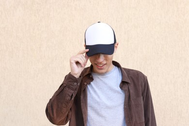 Photo of Smiling man in stylish baseball cap near beige wall. Mockup for design