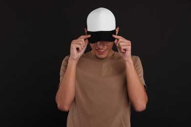 Photo of Smiling man in stylish baseball cap on black background. Mockup for design