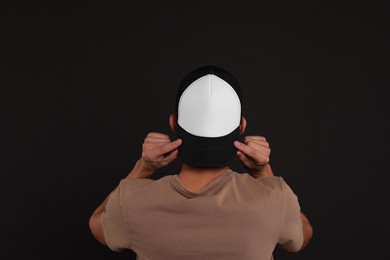 Man in stylish baseball cap on black background, back view. Mockup for design