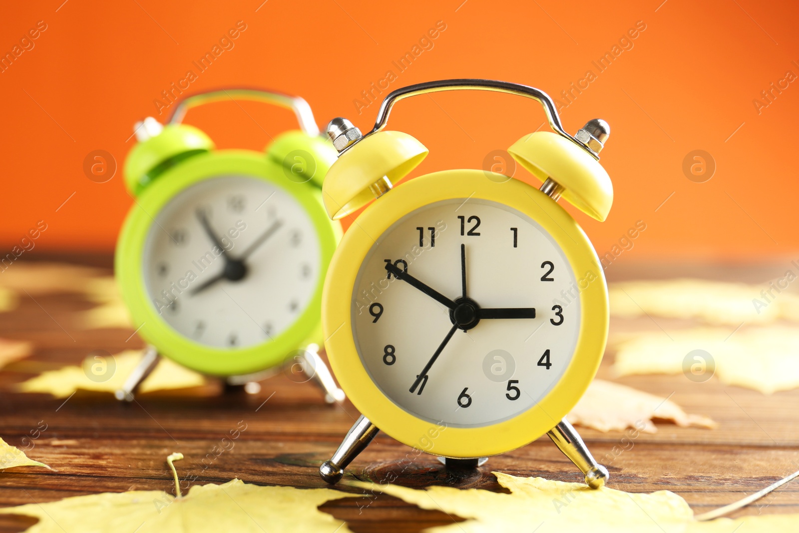 Photo of Autumn time. Alarm clocks and golden leaves on wooden table, selective focus