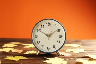 Photo of Autumn time. Alarm clock and golden leaves on wooden table