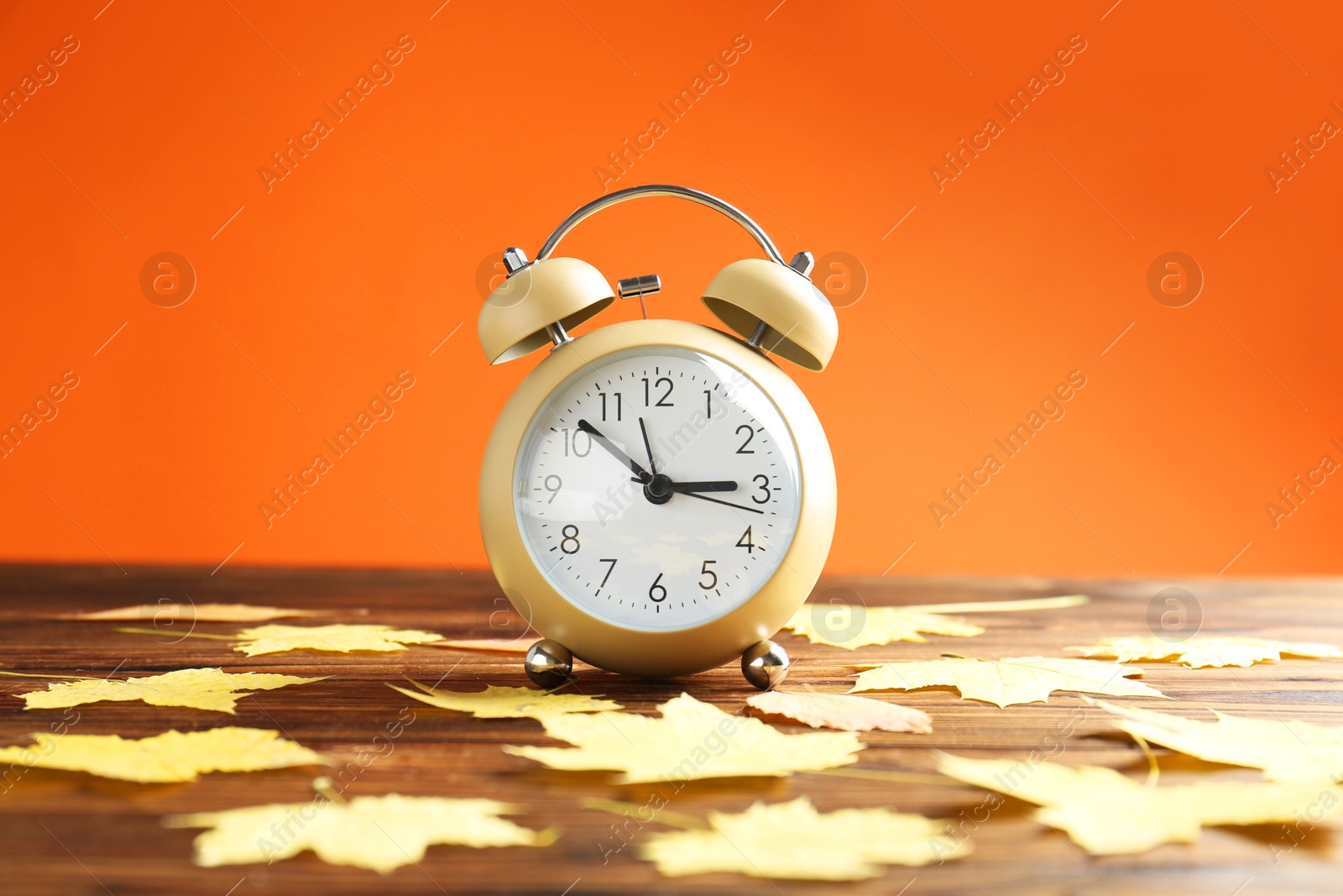 Photo of Autumn time. Alarm clock and golden leaves on wooden table