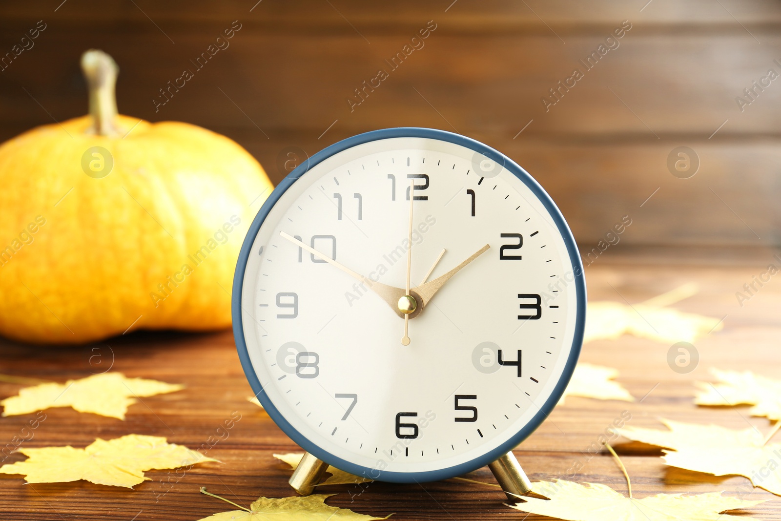 Photo of Autumn time. Alarm clock and golden leaves on wooden table