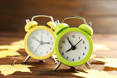 Photo of Autumn time. Alarm clocks and golden leaves on wooden table, selective focus