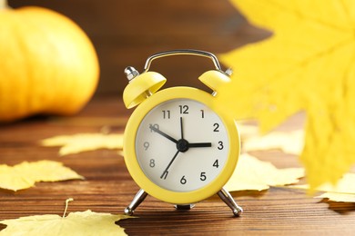 Photo of Autumn time. Alarm clock and golden leaves on wooden table