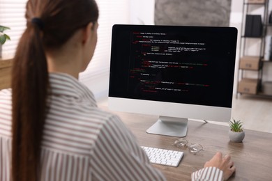 Photo of Programmer working on computer at wooden desk indoors, back view