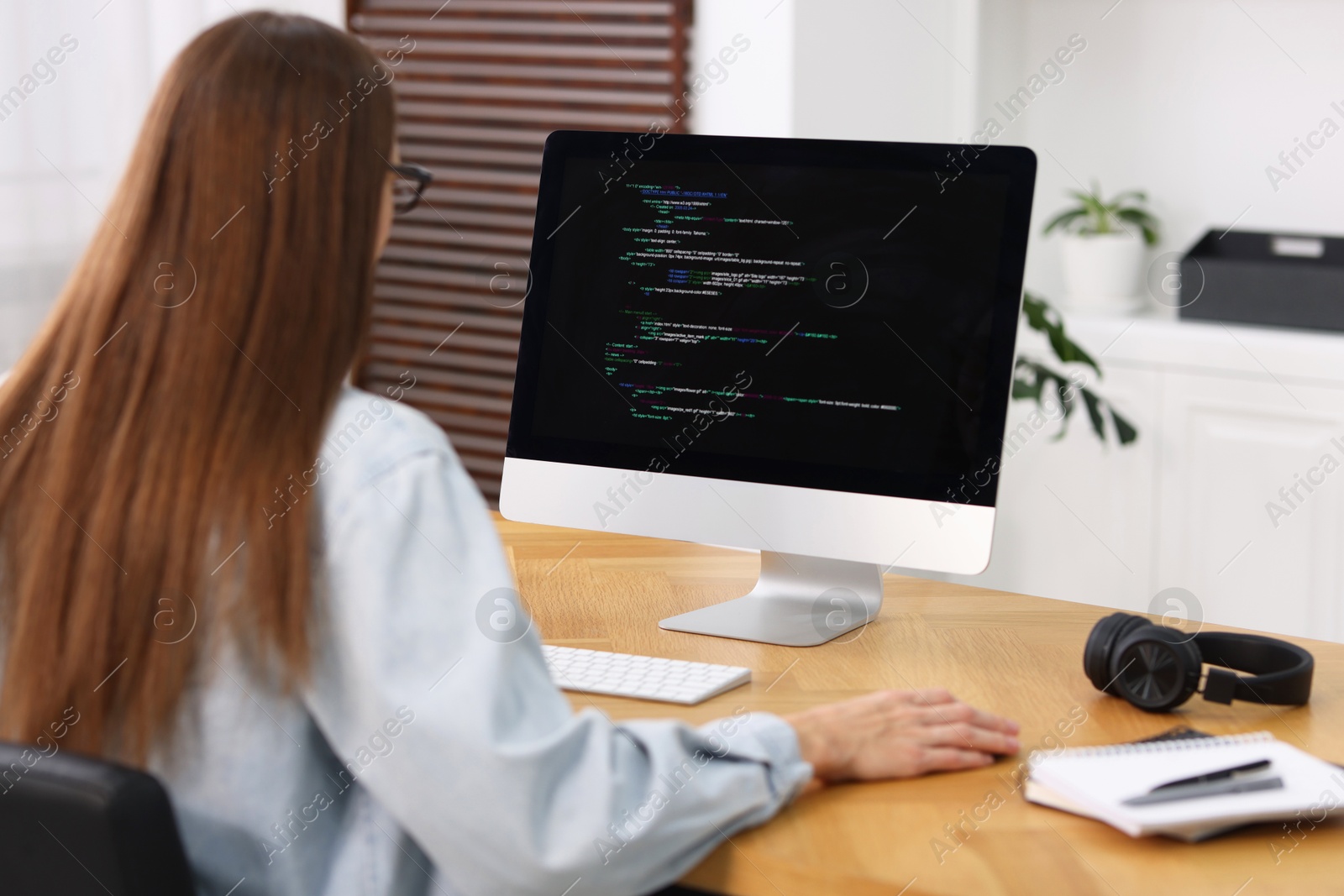 Photo of Programmer working on computer at wooden desk indoors, back view