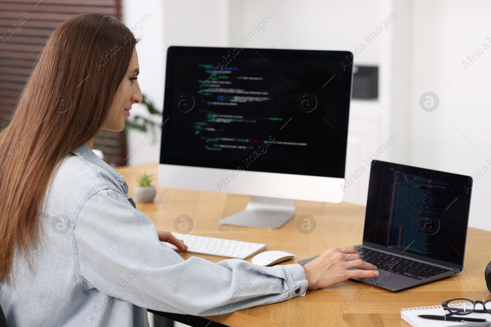 Photo of Programmer working on laptop and computer at wooden desk indoors