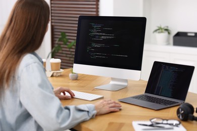 Photo of Programmer working on laptop and computer at wooden desk indoors, back view