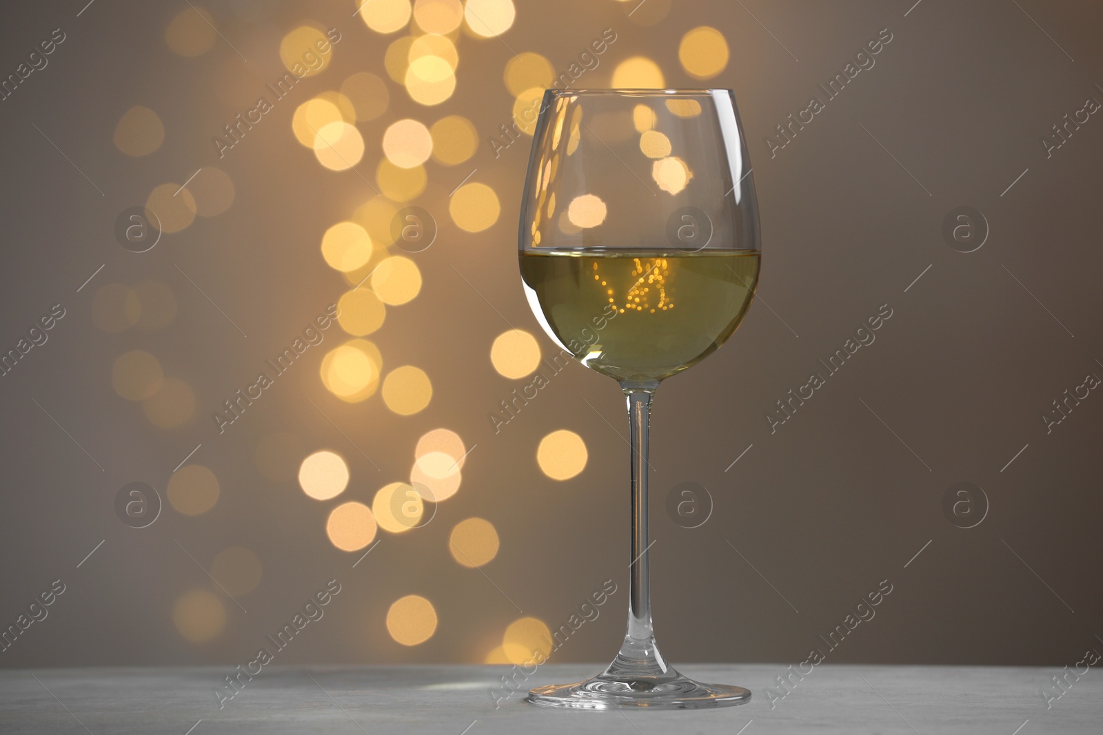 Photo of Tasty white wine in glass on table against grey background with blurred lights, bokeh effect. Space for text