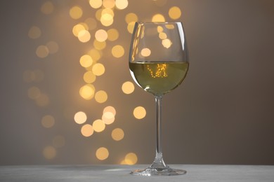 Tasty white wine in glass on table against grey background with blurred lights, bokeh effect. Space for text