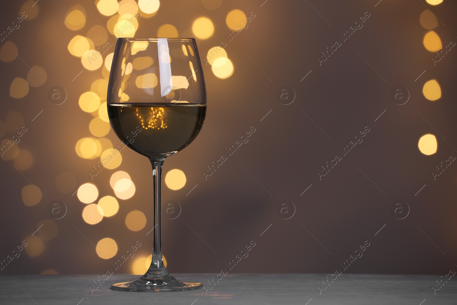 Photo of Tasty white wine in glass on table against dark grey background with blurred lights, bokeh effect. Space for text