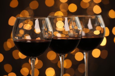 Photo of Tasty red wine in glasses against dark background with blurred lights, closeup. Bokeh effect