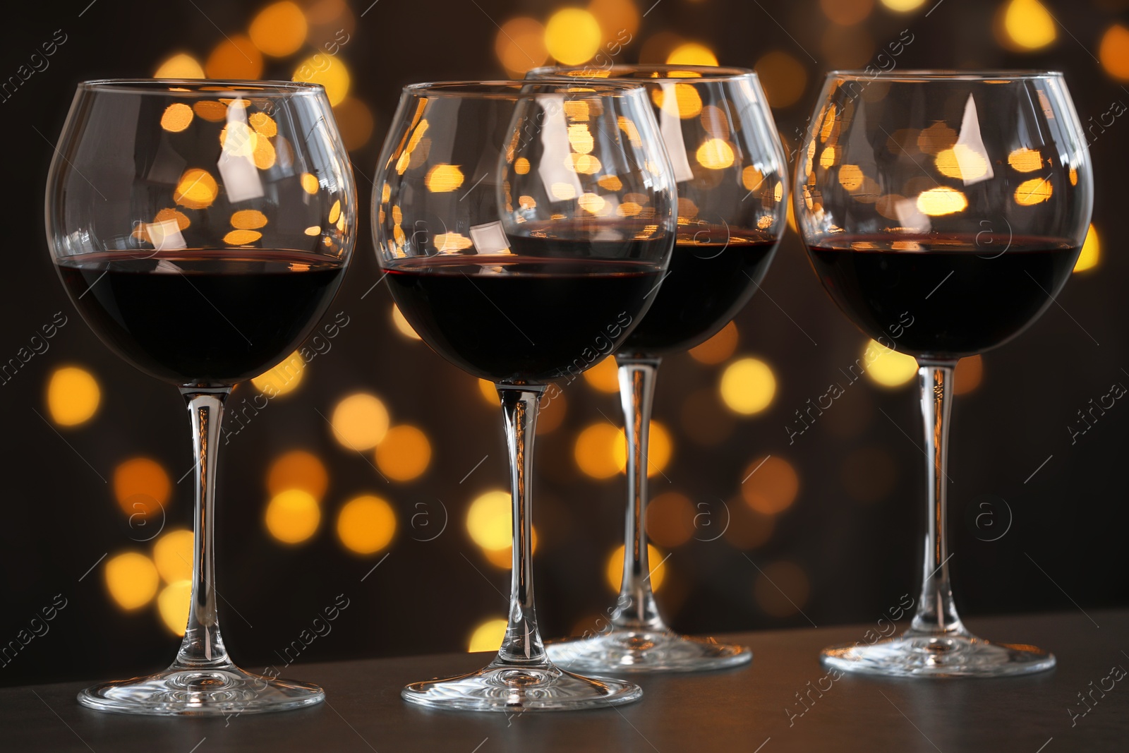 Photo of Tasty red wine in glasses on table against dark background with blurred lights, bokeh effect