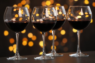 Photo of Tasty red wine in glasses on table against dark background with blurred lights, bokeh effect