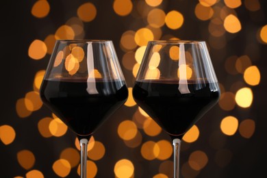 Photo of Tasty red wine in glasses against dark background with blurred lights, closeup. Bokeh effect