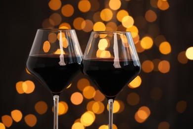 Photo of Tasty red wine in glasses against dark background with blurred lights, closeup. Bokeh effect