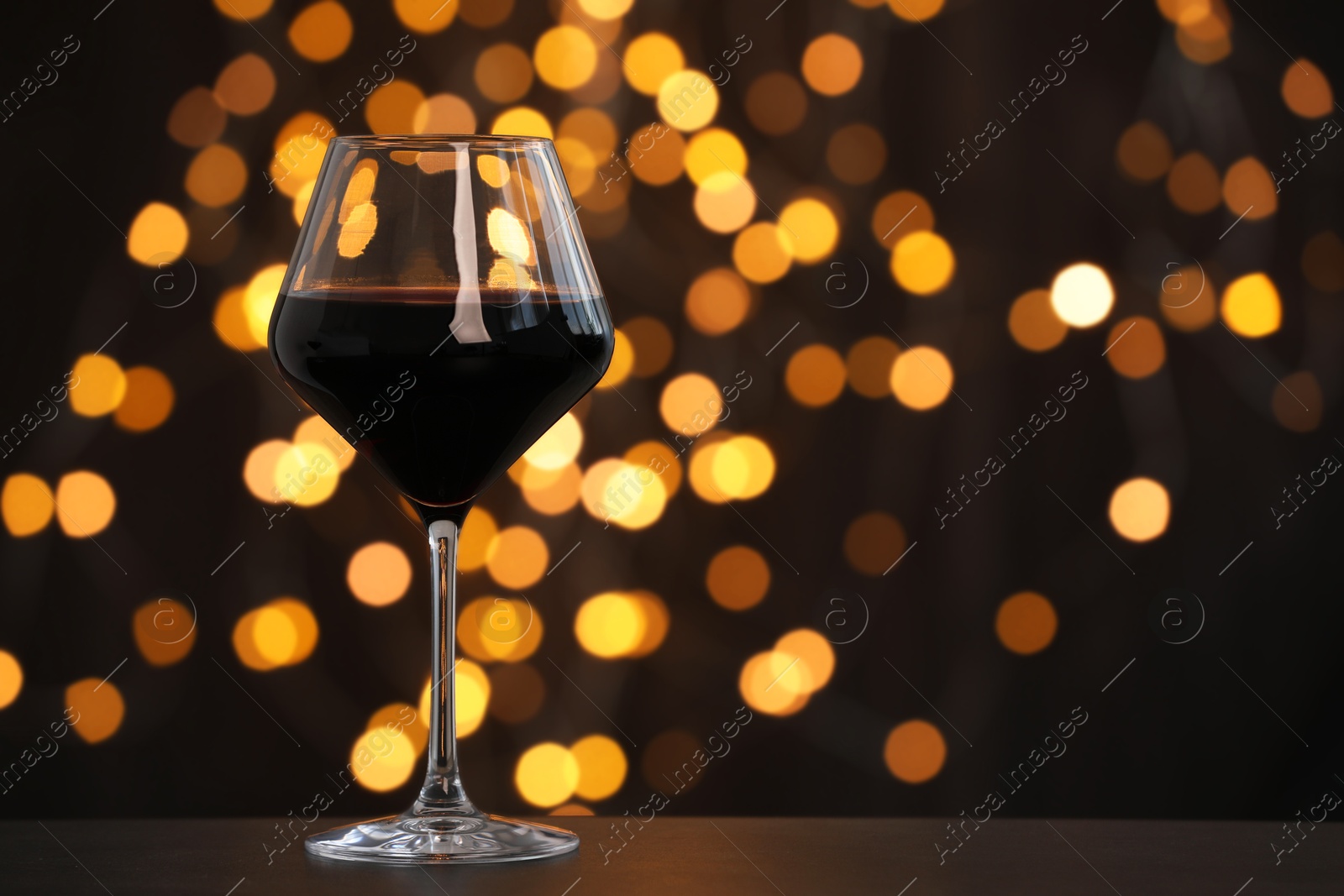 Photo of Tasty red wine in glass on table against dark background with blurred lights, bokeh effect. Space for text